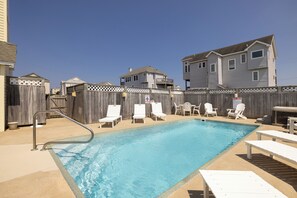 A backyard with a swimming pool, lounge chairs, and a wooden fence. - Ocean Escape: Oceanside, pool, hot tub, pool table, easy beach access (Kill Devil Hills)
