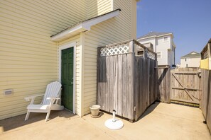 Un jardin à l’arrière d’une maison, avec une clôture en bois, une porte verte, une chaise blanche et un pot de fleurs.