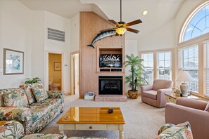 Un salon avec une cheminée, un ventilateur de plafond et une grande fenêtre.