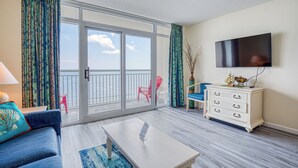 A room with a sofa, a coffee table, a TV mounted on the wall, a white dresser, and a balcony with a view of the sea. - Oceanfront 1BD-Baywatch Resort-Family Friendly (North Myrtle Beach)