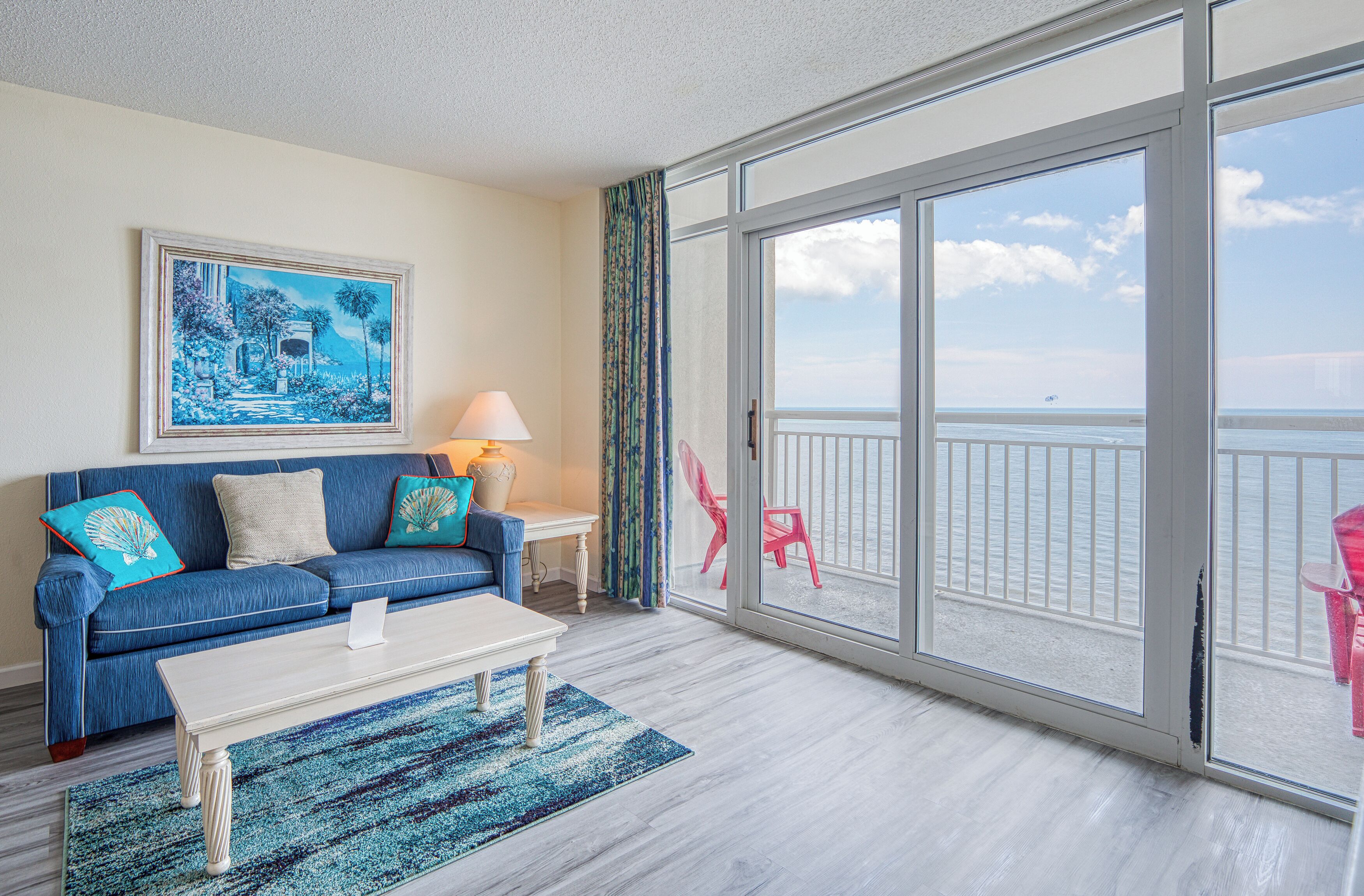 A room with a blue sofa, a white coffee table, and a view of the ocean through large glass doors.