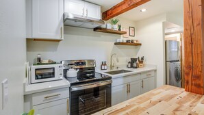 Cucina con mobili bianchi, piano cottura in acciaio inossidabile, forno a microonde e ripiano in legno.