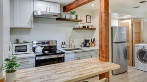 Una cucina moderna con mobili bianchi, un piano di lavoro in legno, elettrodomestici in acciaio inossidabile e un soffitto con travi in legno.
