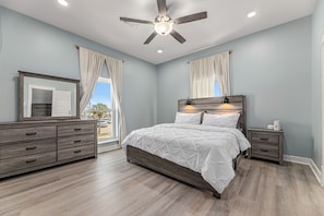Un dormitorio con cama, cómoda, mesita de noche, ventilador de techo y ventana con cortinas.