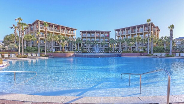 A hotel with a large pool, multiple balconies, and palm trees.