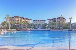 Un hotel con una piscina grande, varios balcones y palmeras.
