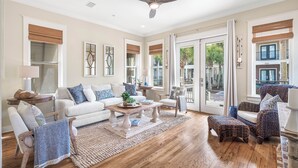 A spacious living room with a white sofa, patterned armchairs, a wooden coffee table, and a large window with a view of the outdoors.