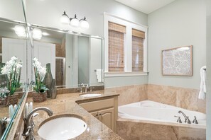 Un baño moderno con un espejo grande, dos lavamanos, una bañera y plantas decorativas.