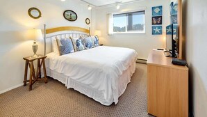 Une chambre à coucher avec un lit, une table de chevet, une lampe et une œuvre d’art accrochée au mur.