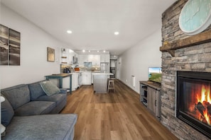 Una sala de estar moderna con chimenea, una cocina al fondo y un sofá gris.