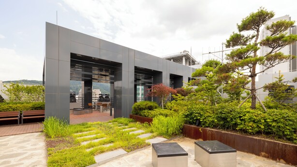 Un bâtiment moderne doté d’une façade en verre, d’un espace extérieur aménagé pour s’asseoir et d’un jardin paysager avec des pierres plates servant de marchepied.