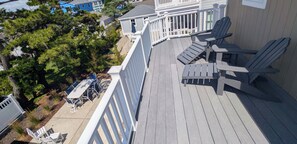 A deck with Adirondack chairs, a white fence, and a view of a residential area with trees and houses.