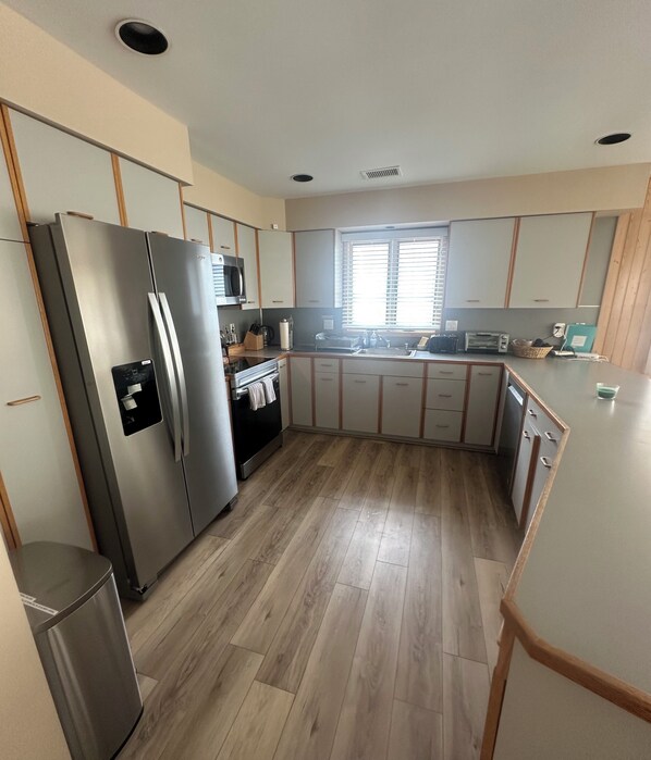 A modern kitchen with a stainless steel refrigerator, wooden cabinets, a microwave, and a window providing natural light.