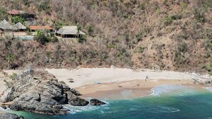 A coastal area with a beach, rocky shoreline, and thatched-roof buildings.