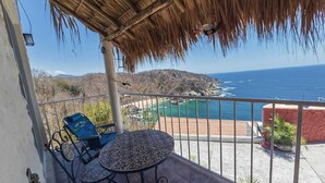 A balcony with a table and chairs, overlooking a coastal view with a beach and mountains.