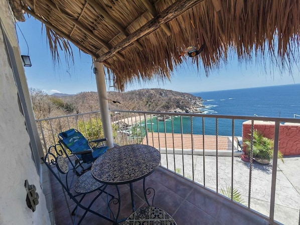 Un balcón con mesa y sillas, con vistas a la costa, una playa y montañas.