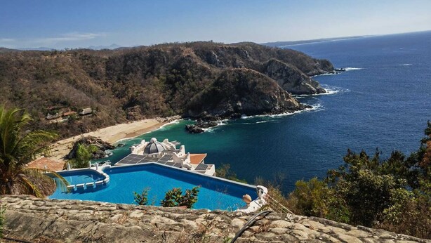 A coastal property with a swimming pool, a beach, and a view of the ocean.