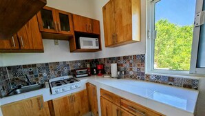 A kitchen with wooden cabinets, a gas stove, a microwave, and a window with a view of greenery.