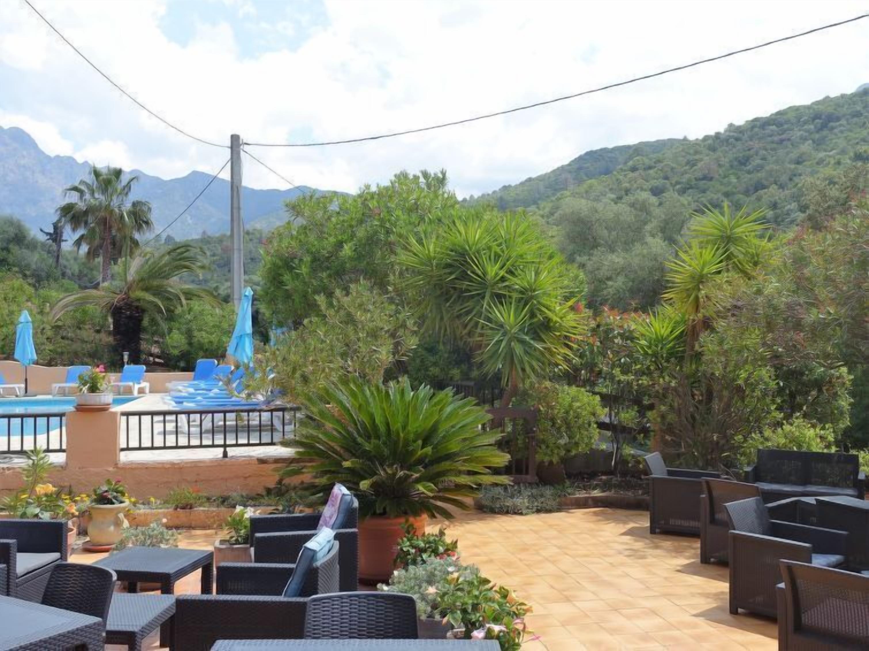 An outdoor patio with lounge chairs and a pool area, surrounded by lush greenery and mountains in the background.
