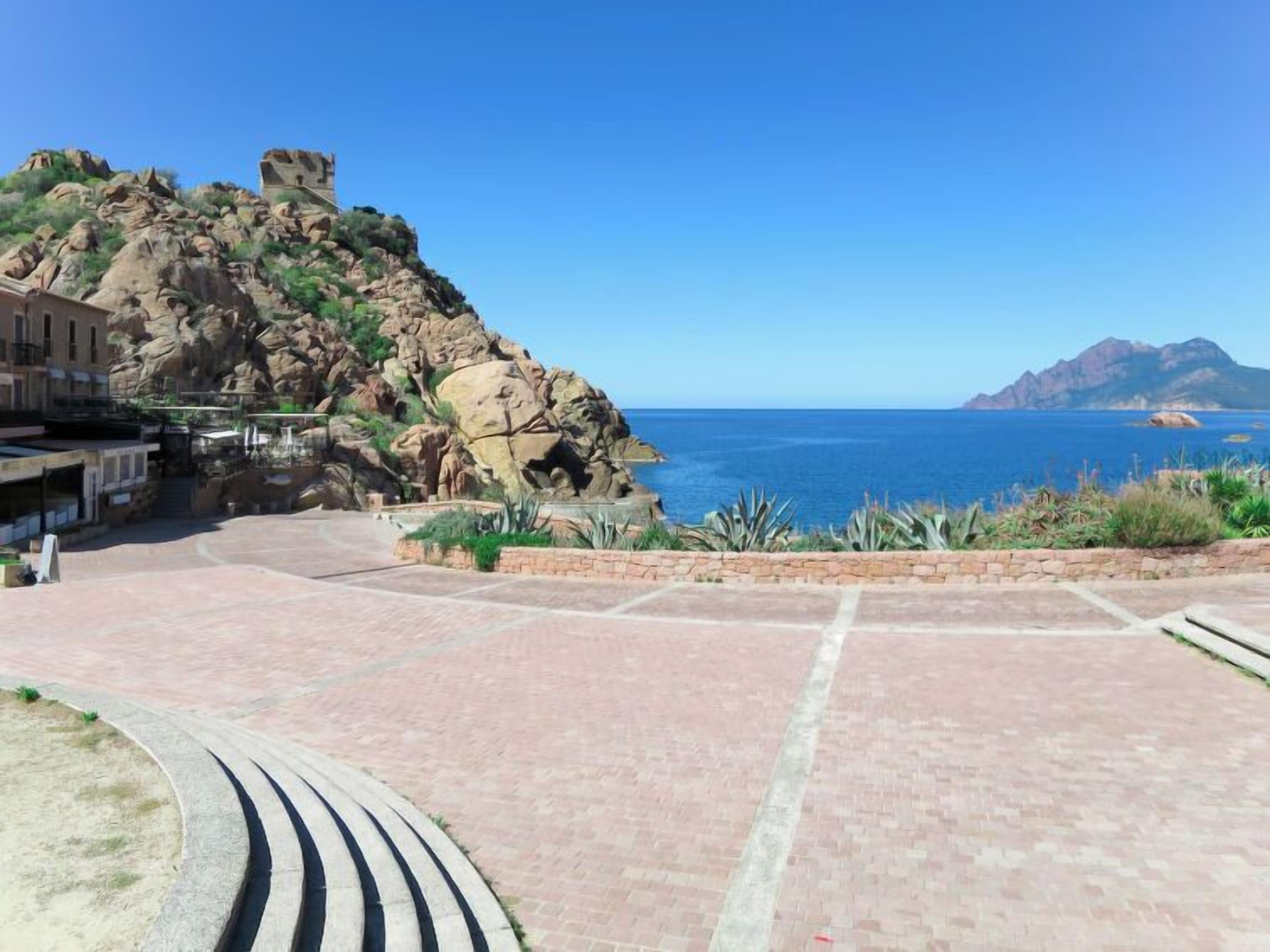 Ein gepflasterter Bereich mit Blick auf das Meer und felsiges Gelände.