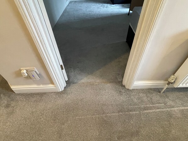 A carpeted hallway with white walls and a door with a lock and a light switch.