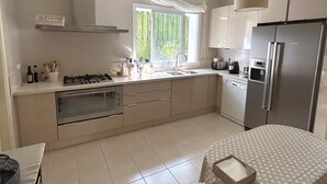 Une cuisine moderne équipée d’une cuisinière à gaz, d’un four et d’un réfrigérateur Bosch. Une fenêtre offre une vue sur la verdure environnante.