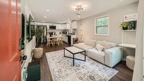 A modern living room with a sofa, coffee table, and a rug. There is a kitchen in the background with cabinets and a dining area. - Nashville Charmer (Nashville)