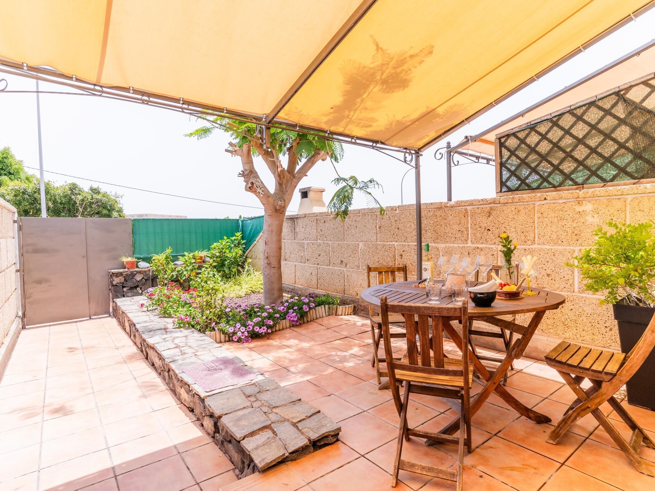 Un patio con mesa y sillas, un árbol y plantas en macetas.