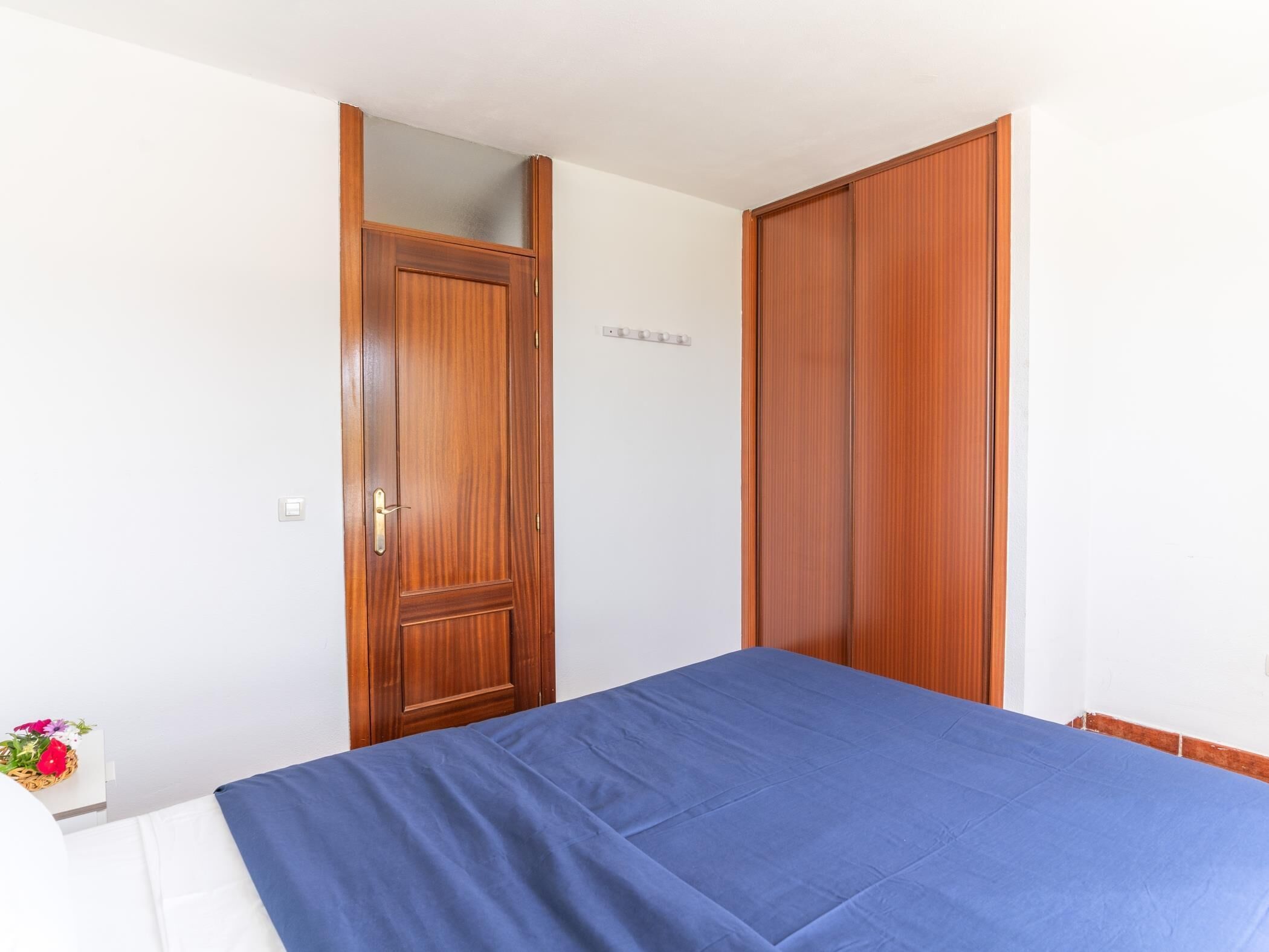 A bedroom with a bed, a wooden wardrobe, and a mirror.