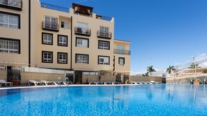 A swimming pool with lounge chairs and a building with multiple balconies in the background. - Beautiful Holiday Home in Costa Adeje with partial sea view (Adeje)