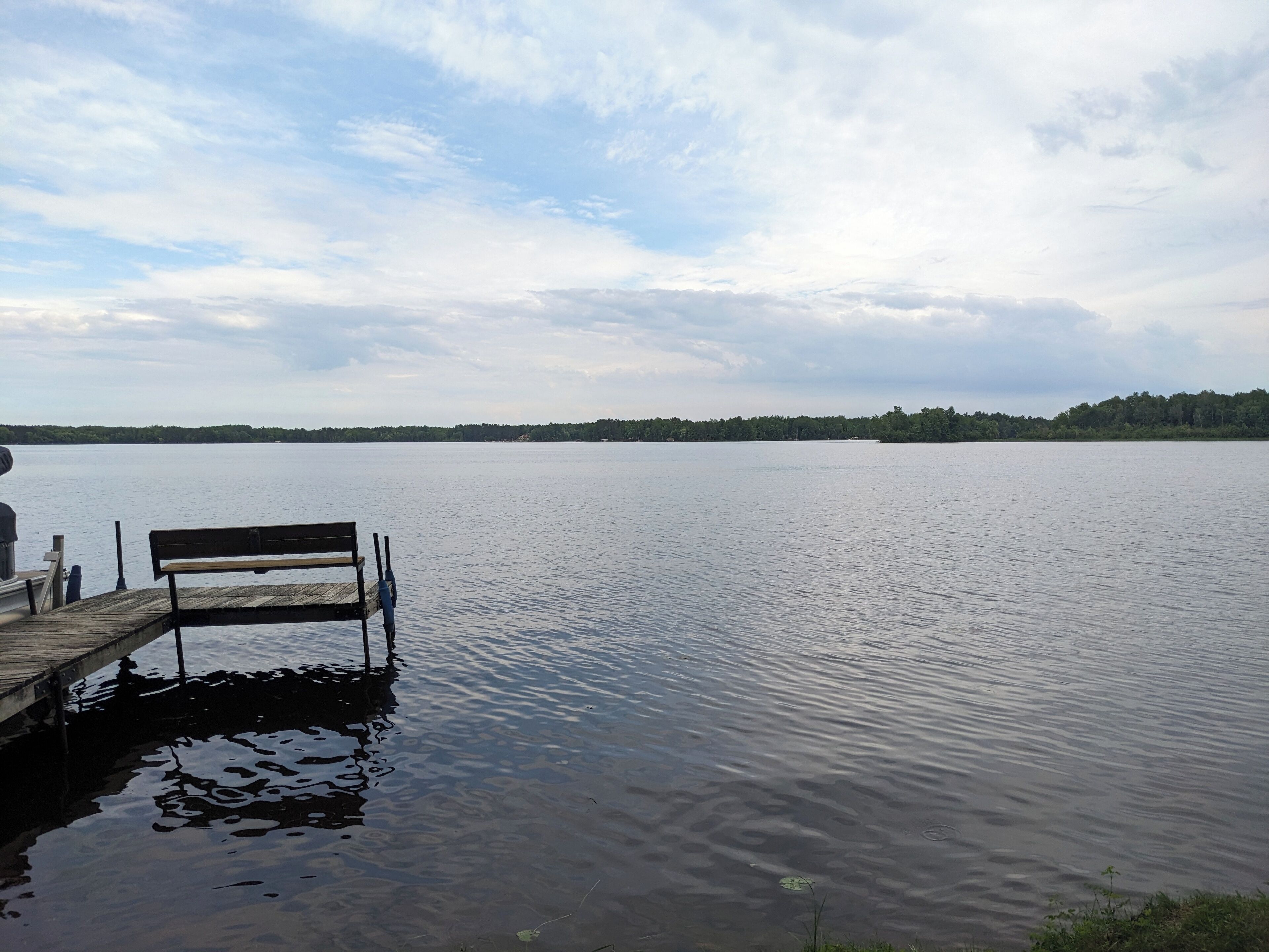 Eine Holzstege, der sich in ruhiges Wasser erstreckt, mit einer Bank am Ende.