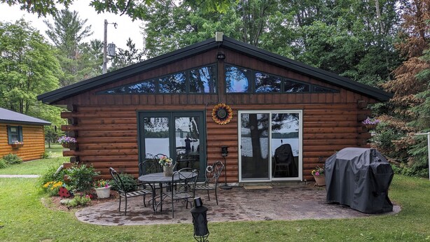 A log cabin with a patio area, a covered grill, and a large window.