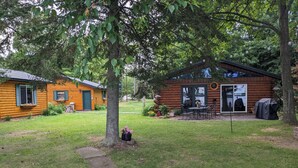 A log cabin with a patio, a covered grill, and a garden area with flowers and plants.