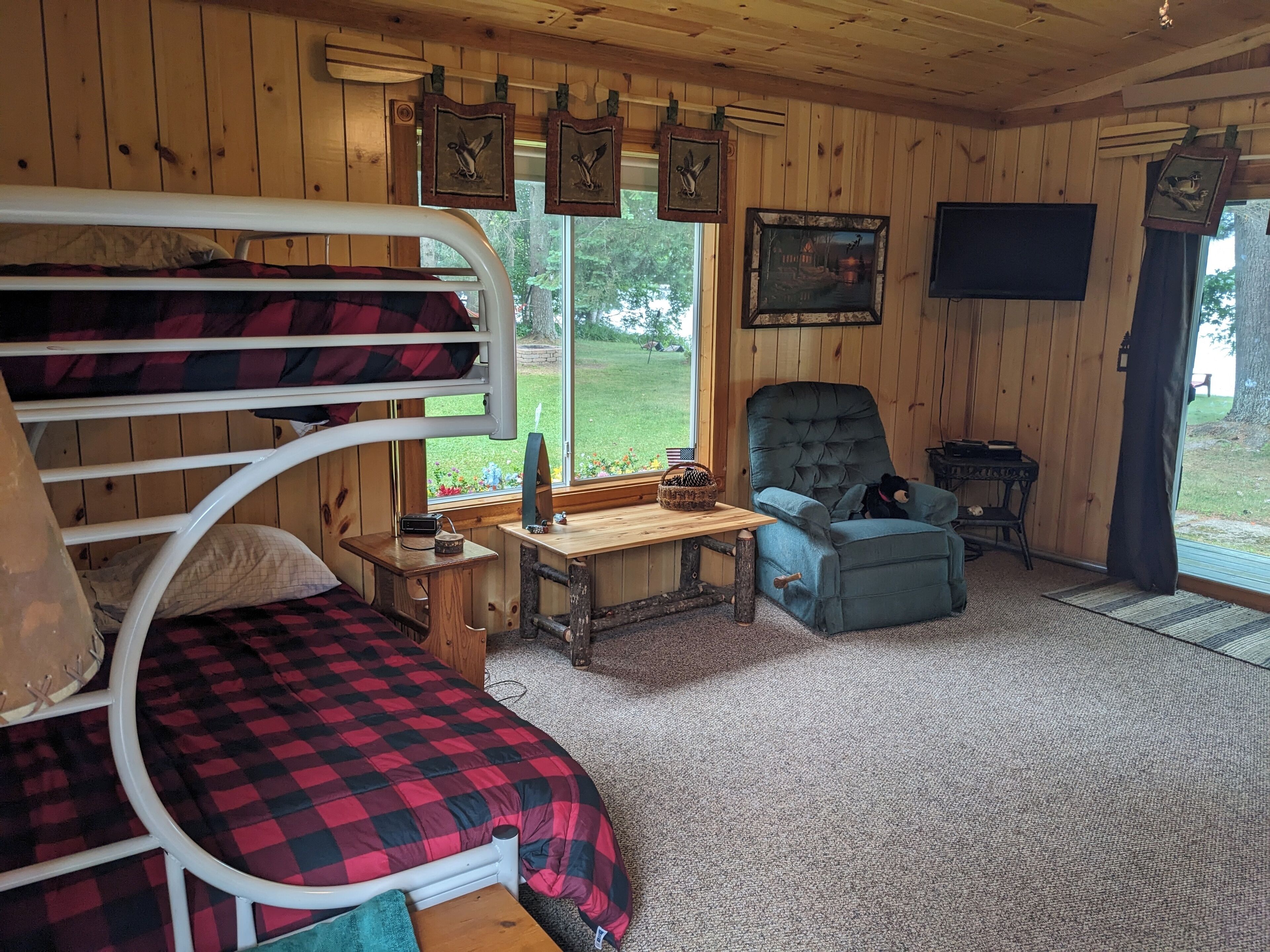 A cozy cabin room with a bunk bed, a chair, a table, and a window offering a view of the outdoors.