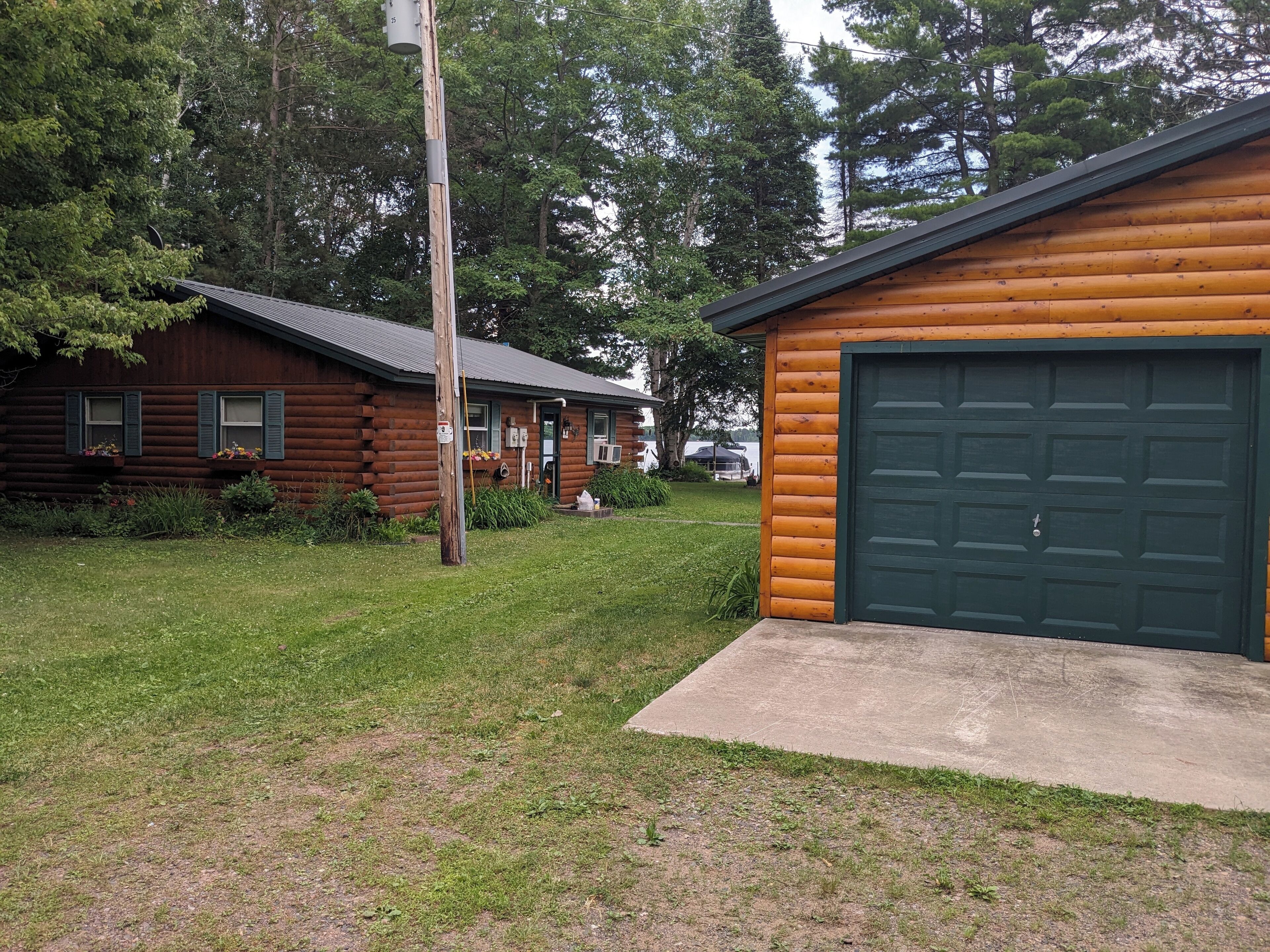 A log cabin with a green garage door, surrounded by a well-maintained lawn and trees.