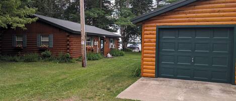 A log cabin with a green garage door, surrounded by a well-maintained lawn and trees.