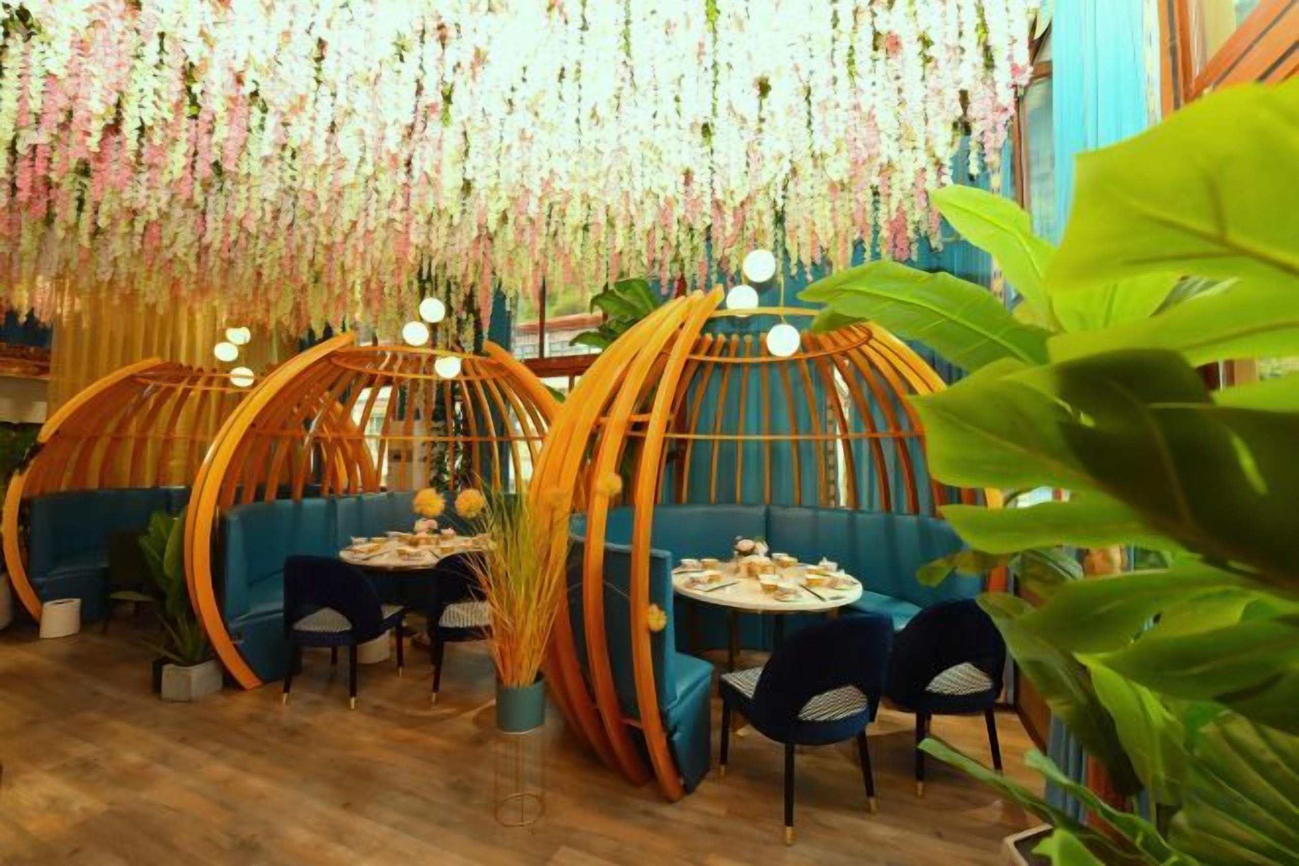 Restaurante com mesas redondas de madeira, assentos azuis e decorações florais pendentes.