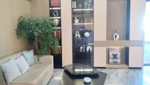A modern living room with a sofa, a coffee table, and a large plant. There is a glass cabinet with various items and a small sculpture on display. - MAERkANG PO LING JIA SA HOTEL (Barkam)