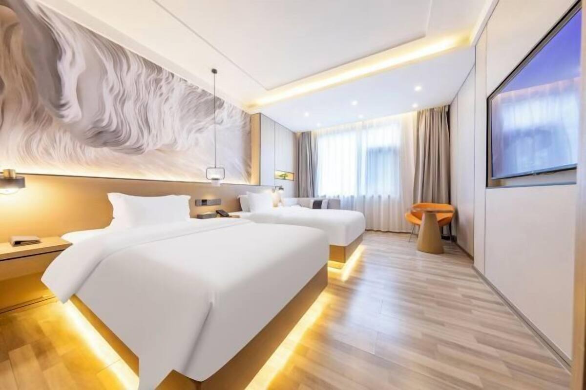 A modern hotel room with two beds, a large abstract wall art, a large window with curtains, and a wooden floor.