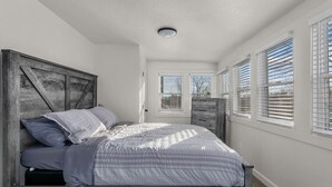 Un dormitorio con cabecera de madera, cama con edredón a rayas y ventana con persianas.