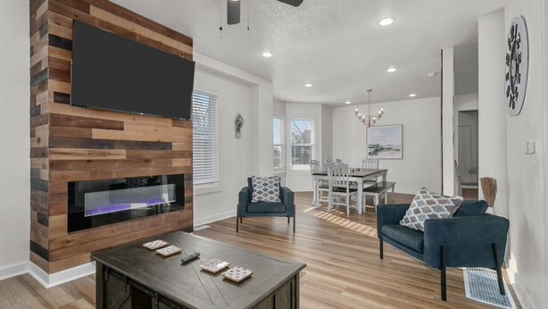 Una sala de estar moderna con un muro decorativo de madera, un televisor de pantalla plana, una chimenea, una zona de comedor con mesa y sillas, y un ventilador de techo.