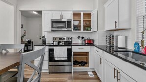 Una cocina moderna con armarios blancos, electrodomésticos de acero inoxidable y una mesa de comedor de madera.