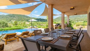 An outdoor dining area with a pool view, wooden furniture, and a table set for a meal.