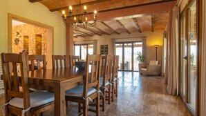 A spacious dining area with a large wooden table and chairs, a stone wall, and a chandelier.