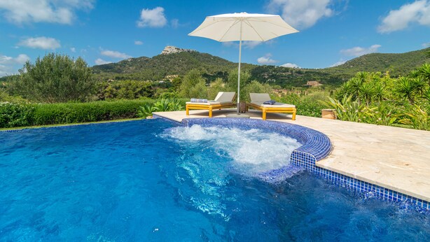 A swimming pool with a hot tub, two lounge chairs, and an umbrella.