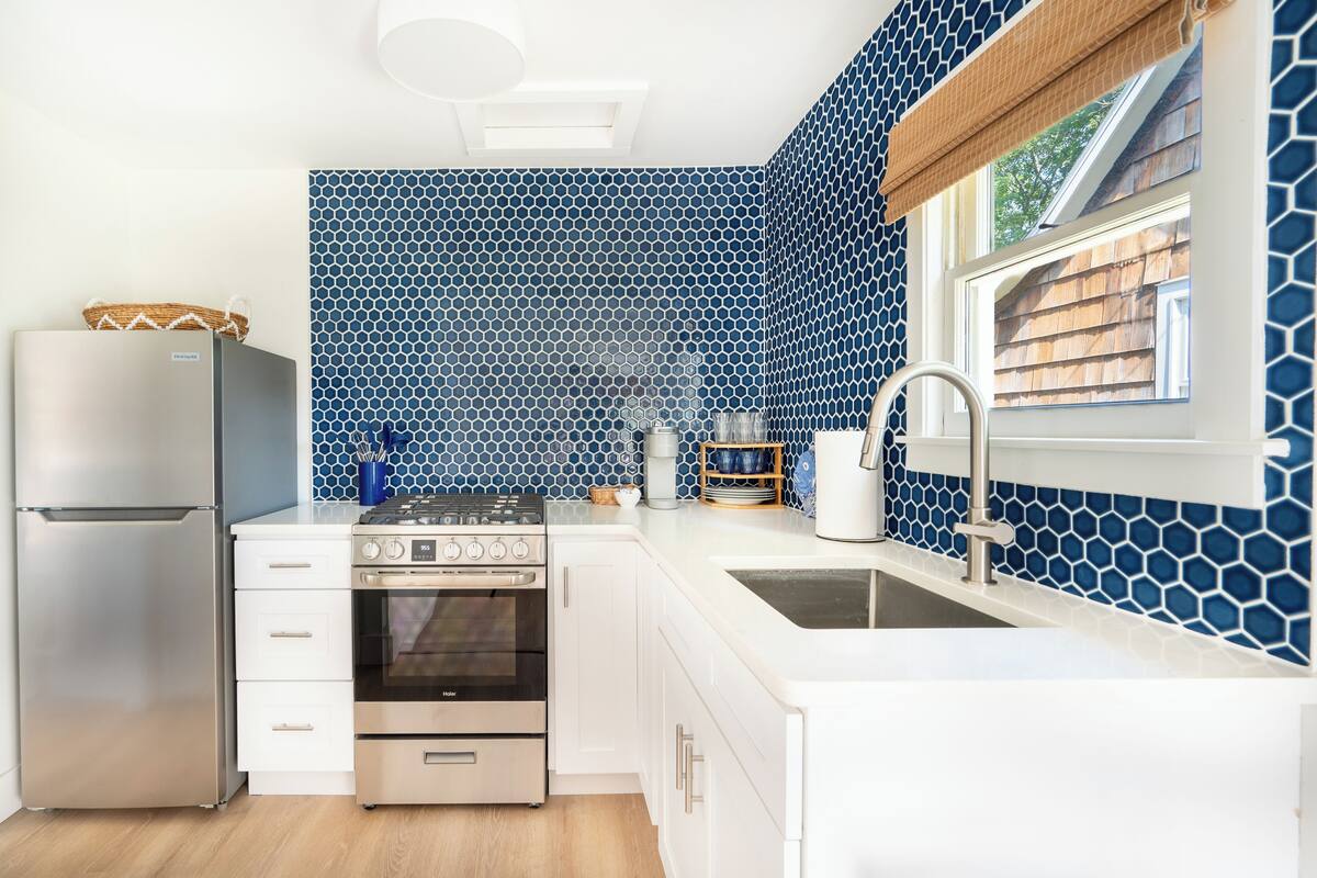Une cuisine moderne avec des meubles blancs, un réfrigérateur en acier inoxydable, une cuisinière à gaz et un évier.