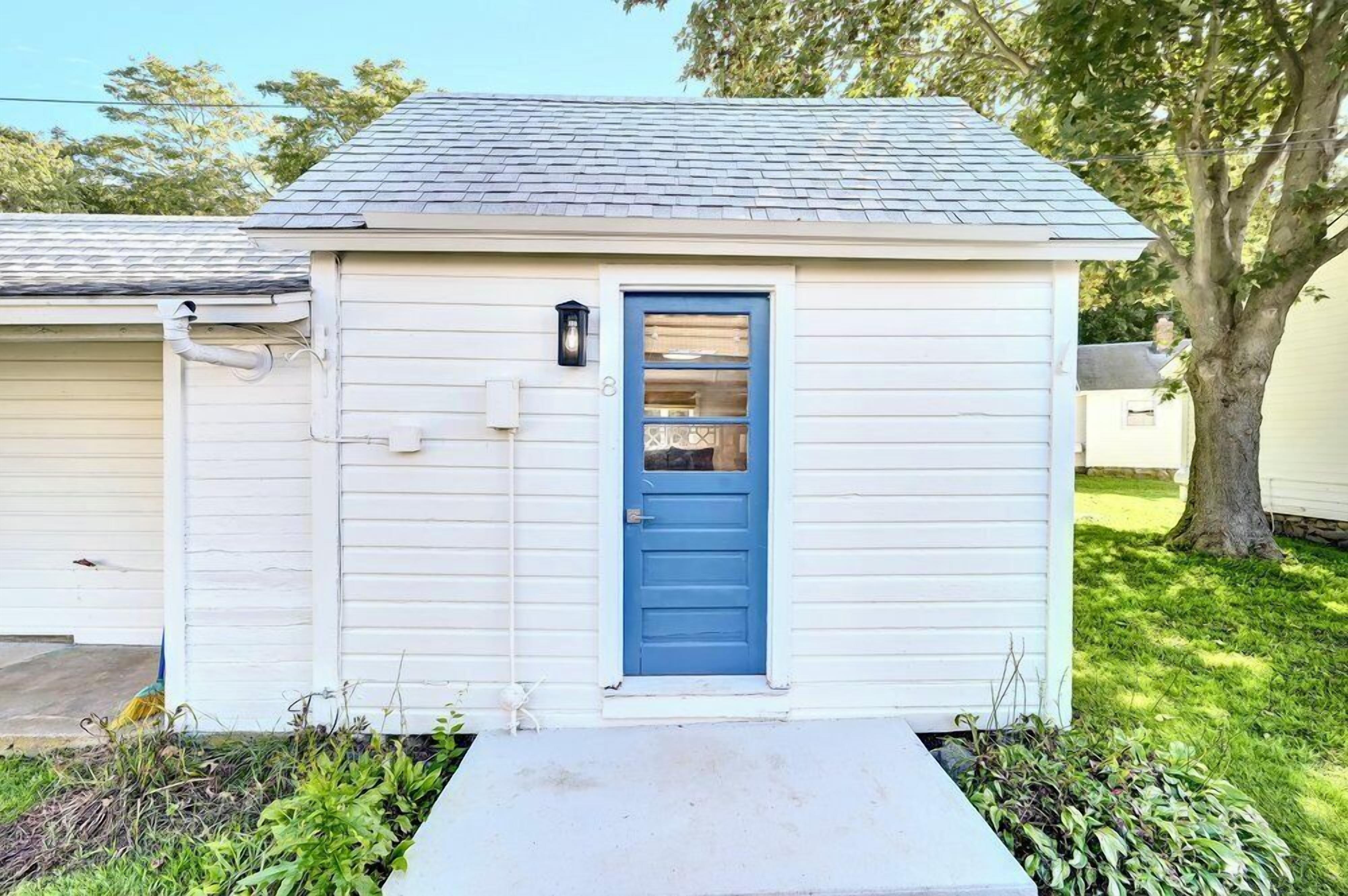 A small, single-story shed with a blue door and a light fixture above it.