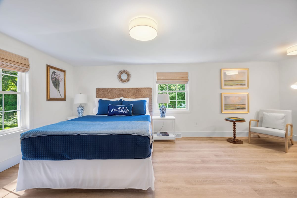 Une chambre avec un grand lit, une table de chevet, une chaise et une fenêtre avec des stores.