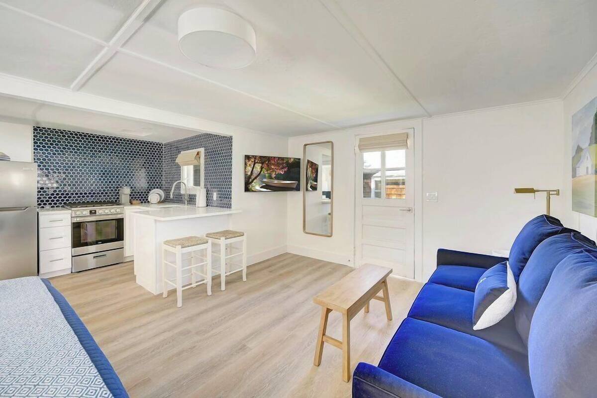 Un espace de vie compact comprenant un coin cuisine, un coin repas et un coin salon avec un canapé bleu et un banc en bois.