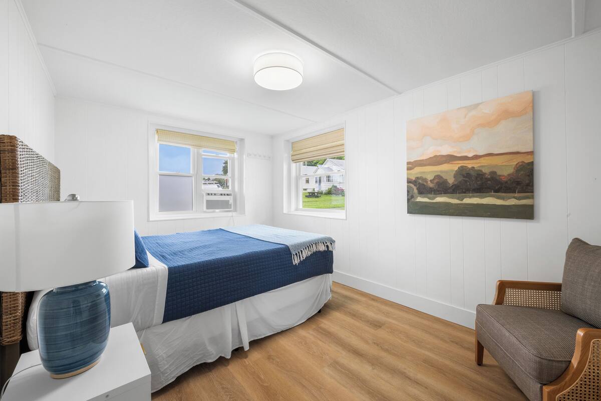 Une chambre à coucher avec un lit, une chaise, une lampe et un tableau au mur.